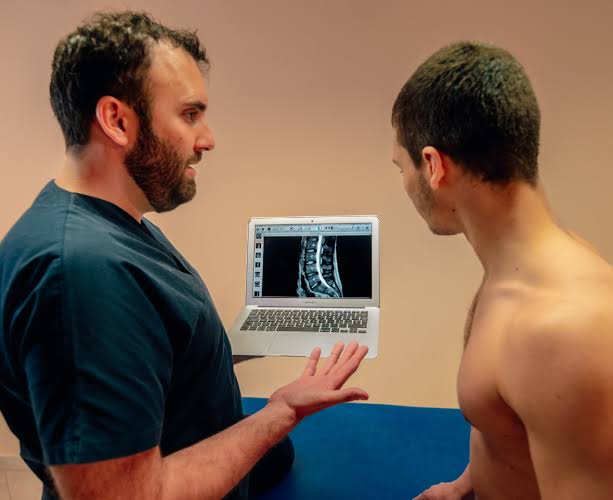 Il Dott. Casari mostra a un paziente la radiografia della colonna vertebrale sul laptop